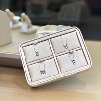 A jewelry display with four small, initial pendant necklaces in a cream-colored tray.