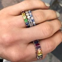 Hand wearing multiple rings, including rainbow-colored gemstone eternity bands.