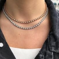 Close-up of a person's neck wearing two diamond tennis necklaces. One is rose gold, the other silver.