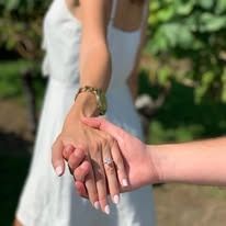 Woman in white dress holding hands, showcasing an engagement ring.