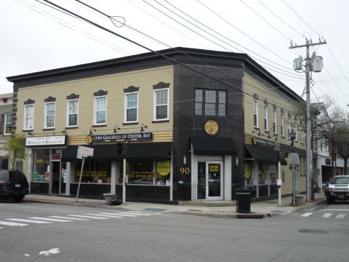 Two-story brick building on a corner, tan facade with black trim, shops on the first floor, street view.