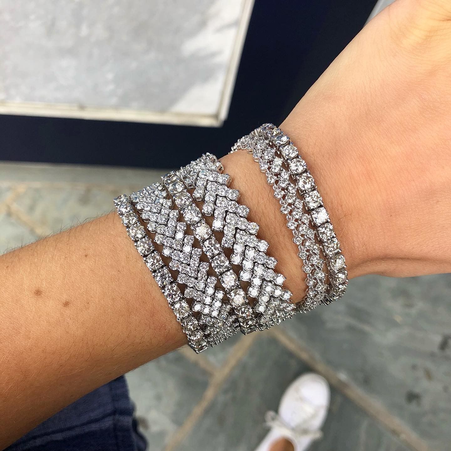 A wrist wearing multiple diamond bracelets, with a chevron design and other sparkling rows.