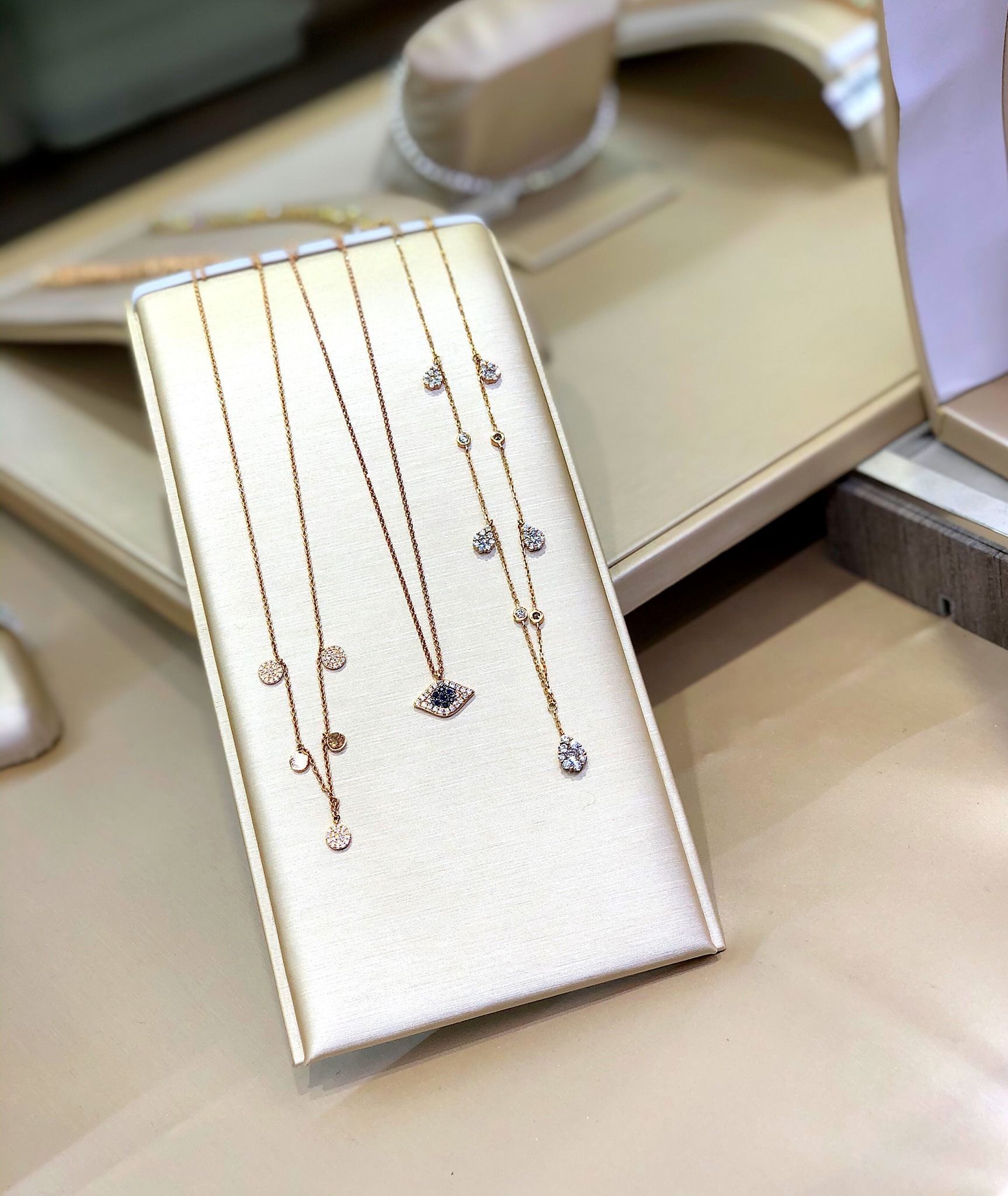 Jewelry display with gold necklaces featuring dangling diamonds on a cream-colored surface.