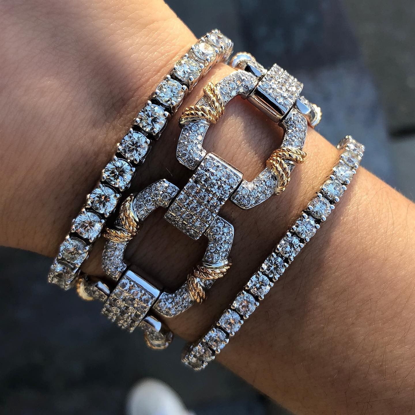 Wrist adorned with four diamond-studded bracelets, including two tennis bracelets and two square clasp designs.