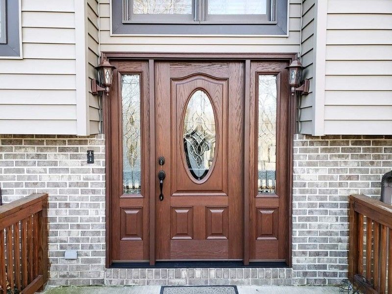 The front door of a brick house with a wooden door and glass windows.