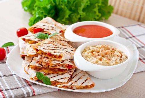 Grilled chicken wrap slices with tomato sauce and dip on a white plate, garnished with lettuce and cherry tomatoes