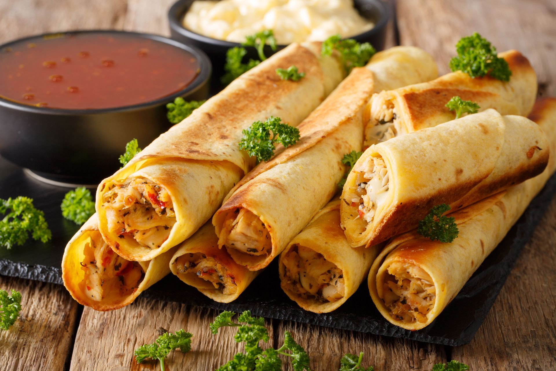 Plate of crispy taquitos with dipping sauce on a wooden table