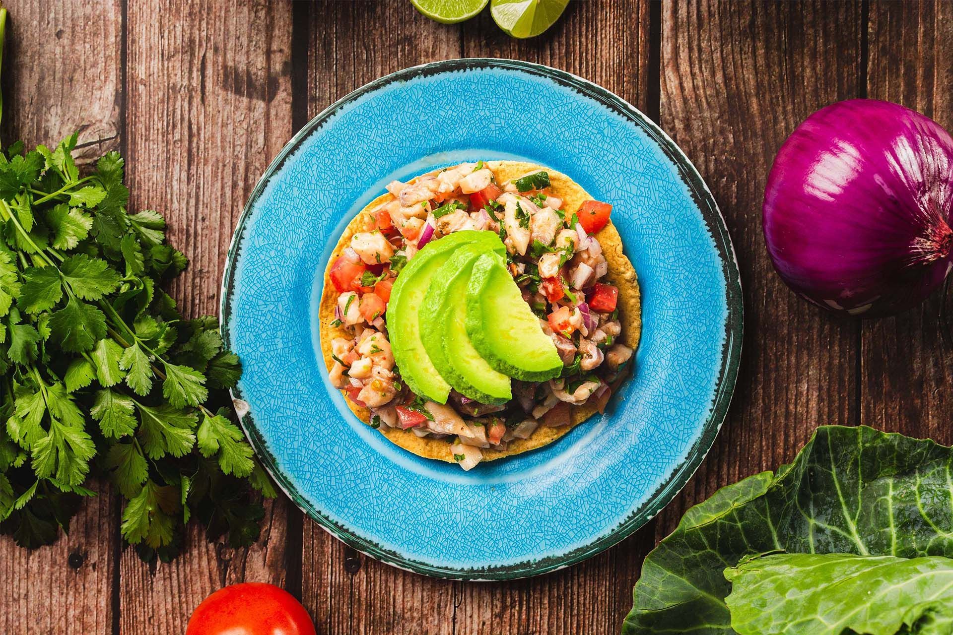 Top-down view of a blue bowl with colorful salsa and avocado on a rustic wooden table