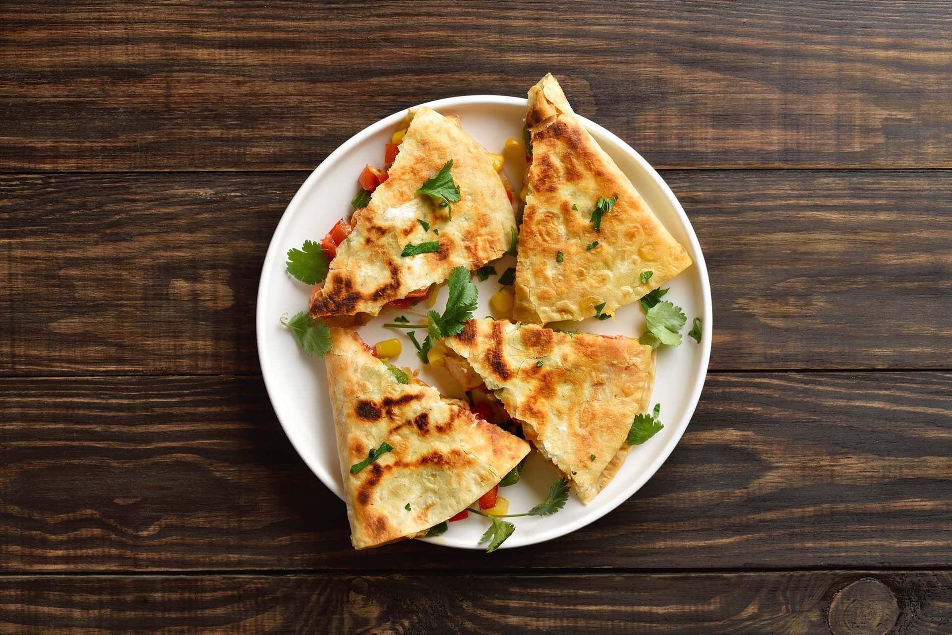 Four triangular slices of golden flatbread on a white plate over a dark wooden table