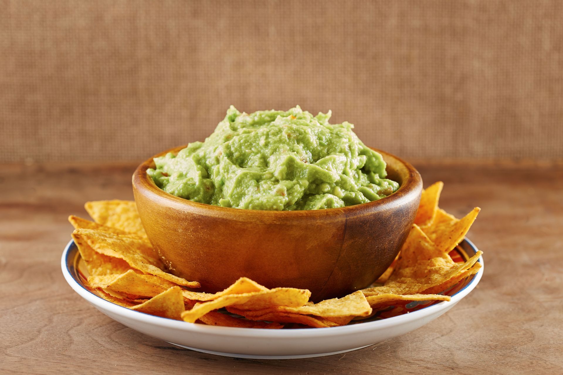 Bowl of guacamole on a plate surrounded by tortilla chips against a brown background