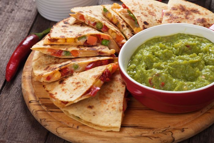 Quesadilla wedges with roasted vegetables and a bowl of green salsa on a wooden board