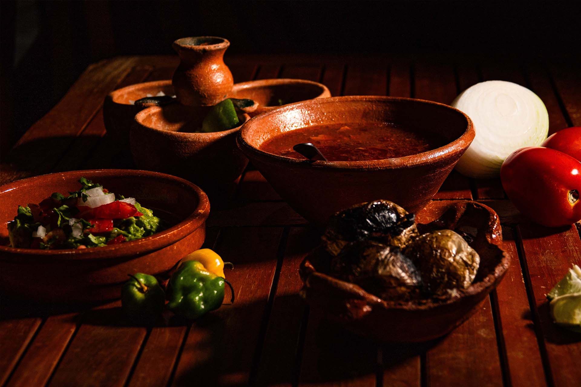 Rustic clay bowls and pots on a wooden table with peppers and onions in warm light