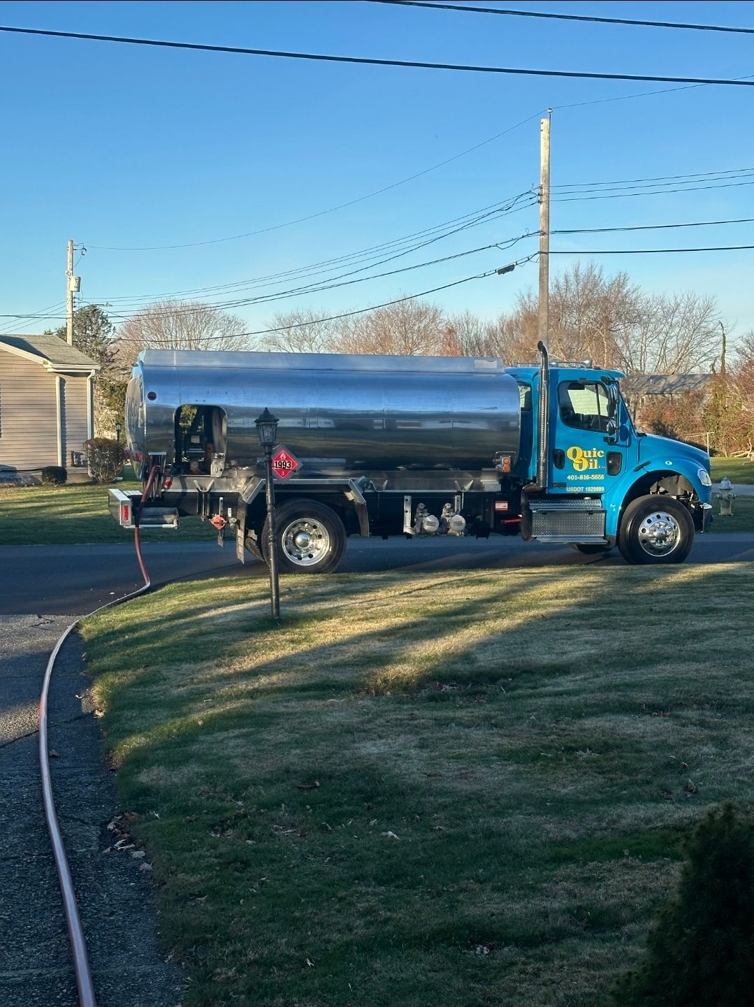 A bright blue oil delivery truck with a large chrome tank parked on a gravel driveway on a sunny day.
