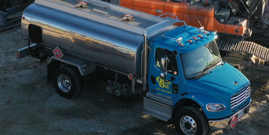 Blue fuel tanker truck at a construction site, silver tank, daytime.