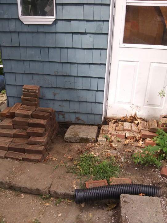 A stack of bricks is sitting in front of a blue house