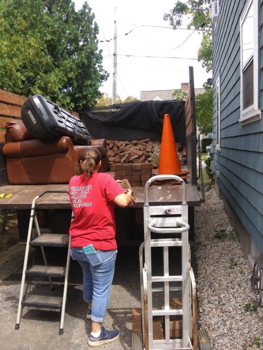 A woman in a red shirt is standing in front of a truck full of furniture