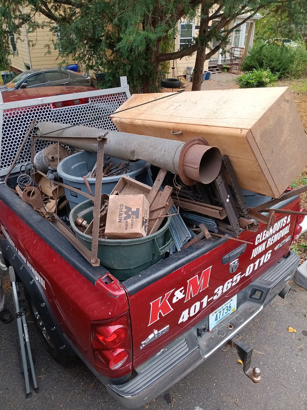 Red pickup truck bed filled with metal scraps, a wooden box, and buckets.