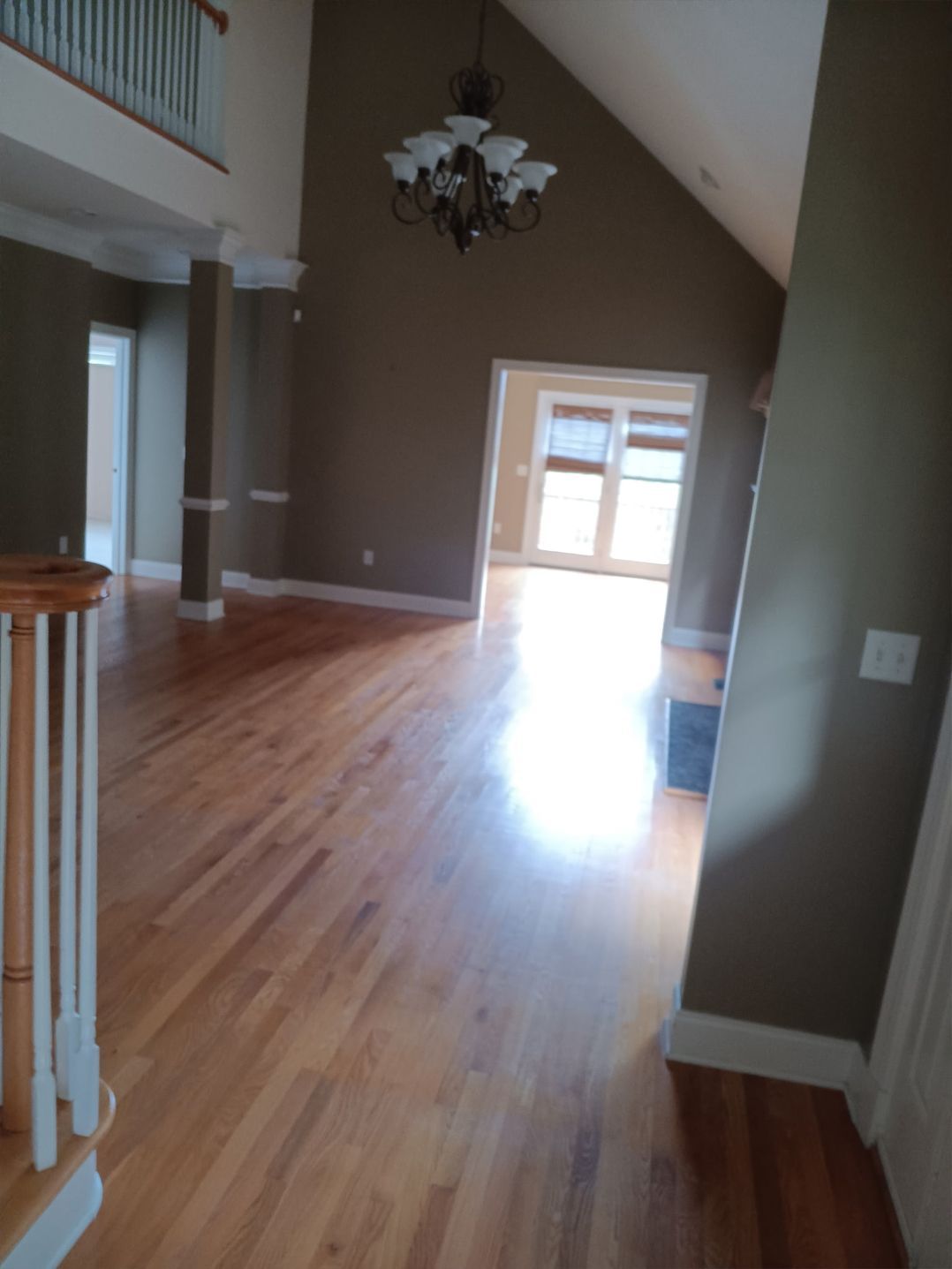 A room with wood flooring and brown walls. A chandelier hangs from the high ceiling.