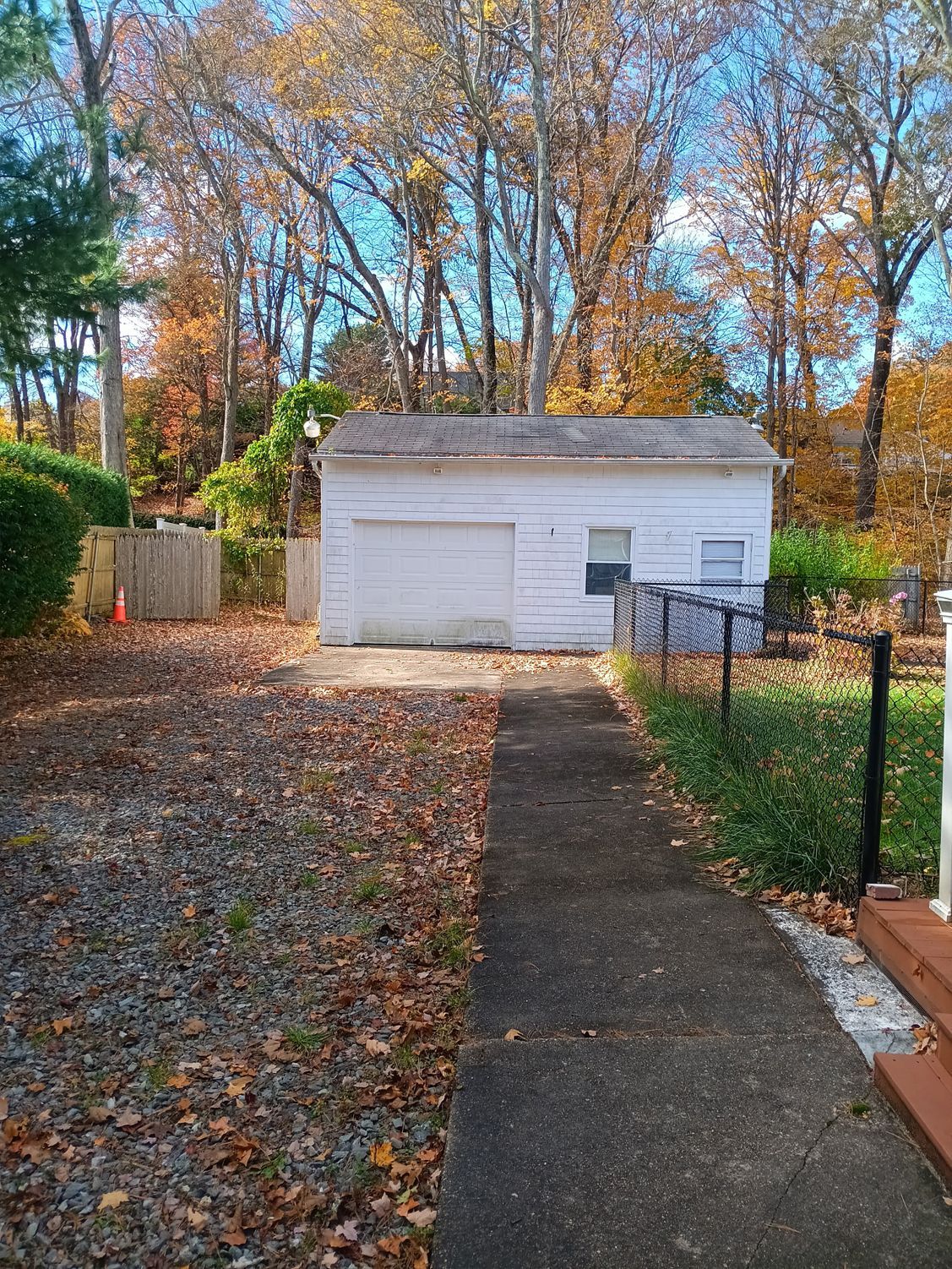 White garage with a closed door, surrounded by trees with fall foliage.