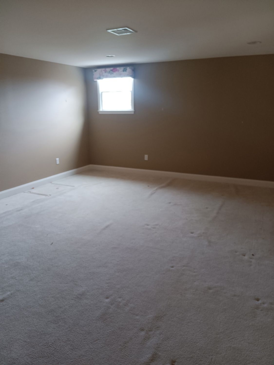 Empty room with tan carpet and brown walls. Small window with a valance.