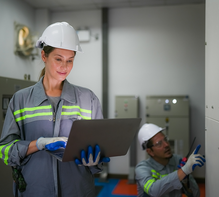 A woman in a hard hat is looking at a laptop computer.