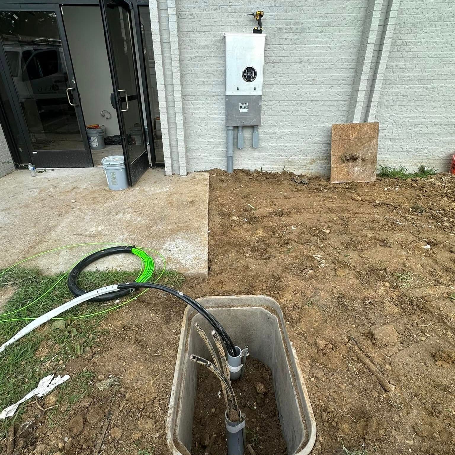 A hose is connected to a box in the dirt in front of a building.