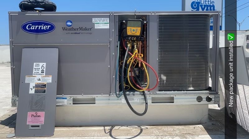 Industrial HVAC unit with open panel and exposed wiring outdoors near a building.