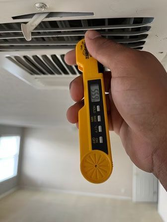 Hand holding a yellow digital thermometer near an air vent, checking airflow temperature