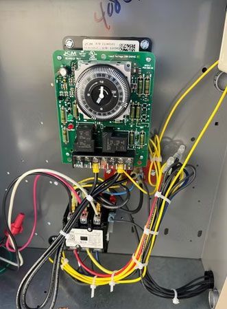 Electrical control panel with timer switch, wiring, and relays mounted inside a metal enclosure