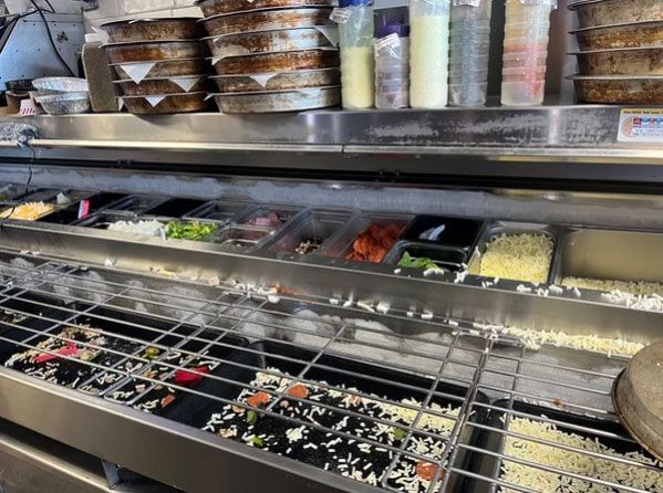 Self-serve salad bar with assorted toppings, dressings, and clear ingredient bins under a metal shelf