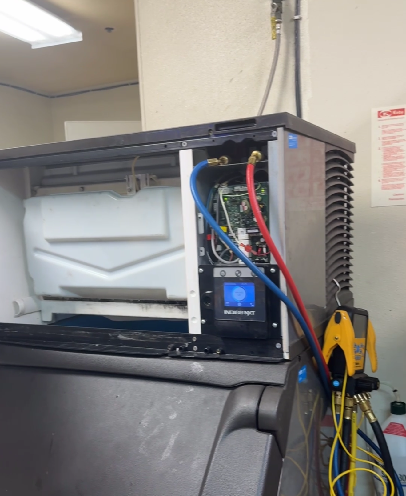 Open electrical control panel with red and blue wires beside a gray machine in a workshop
