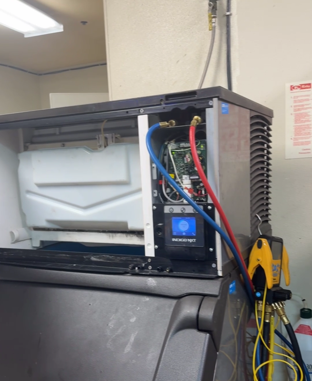 Open electrical control panel with red and blue wires beside a gray machine in a workshop