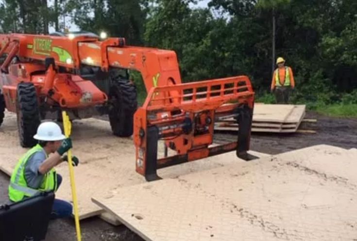Construction workers installing temporary road mats with machinery outdoors.
