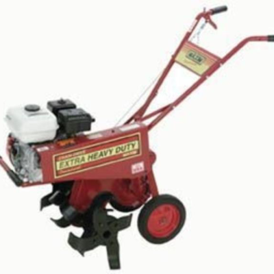 Red, gas-powered tiller with extra heavy duty label, ready for use in a garden.