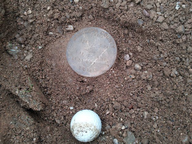 A coin and a golf ball are in the dirt.
