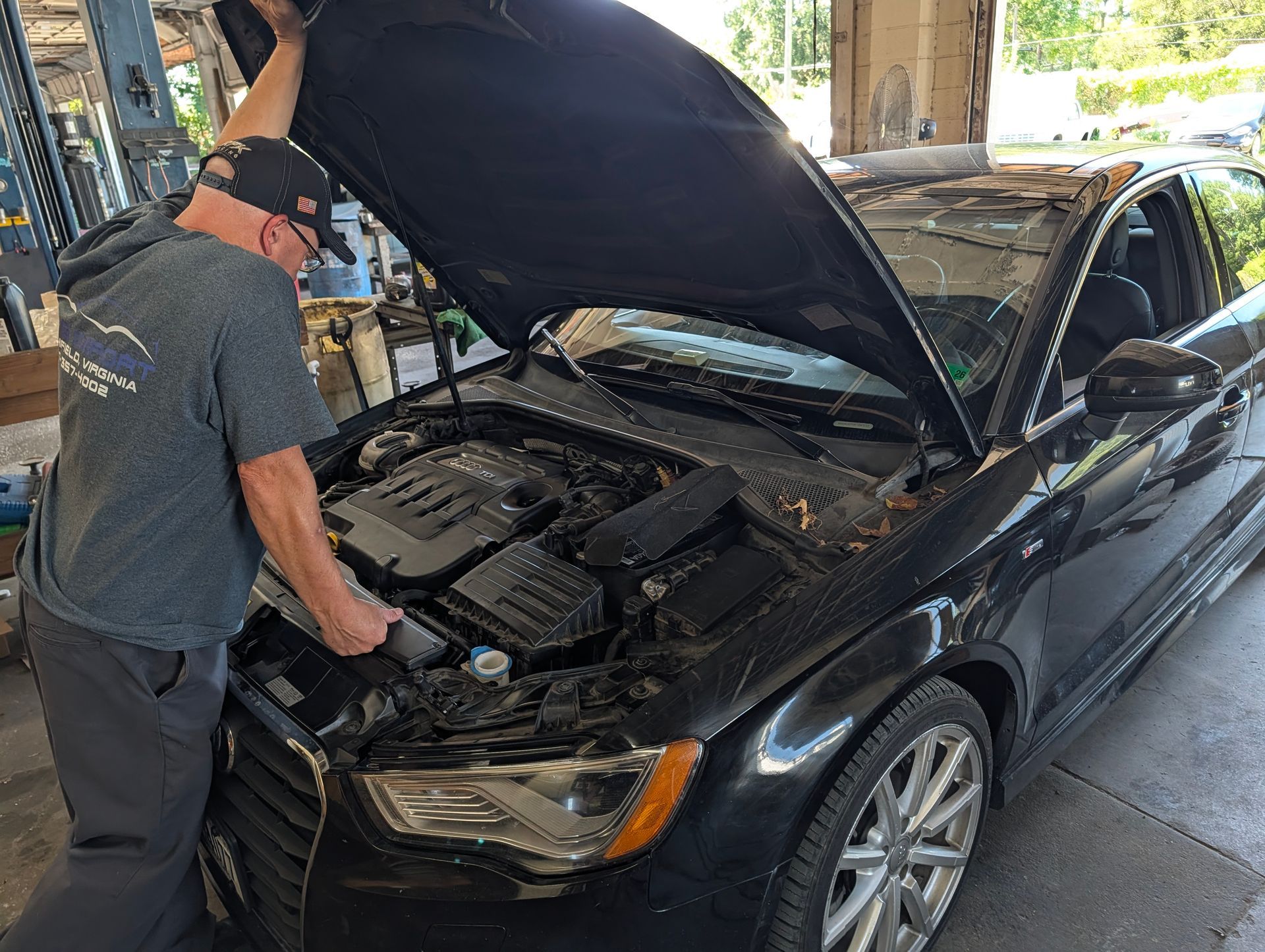 Mechanic inspecting engine under the hood of a black car in a garage
