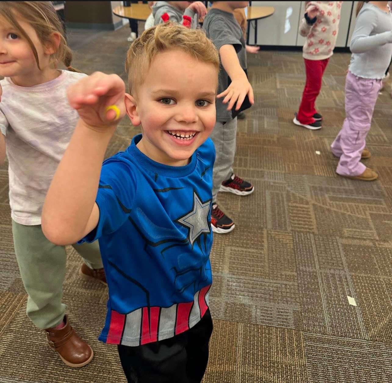 A boy in a captain america shirt is pointing at the camera