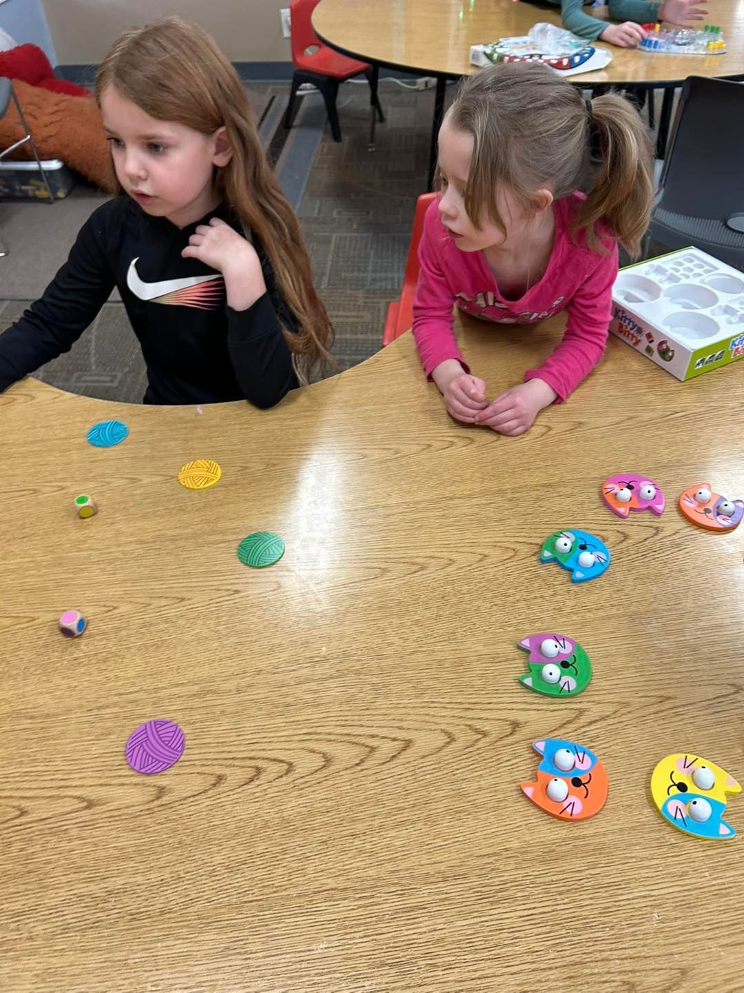 Two young girls are sitting at a table with toys on it.