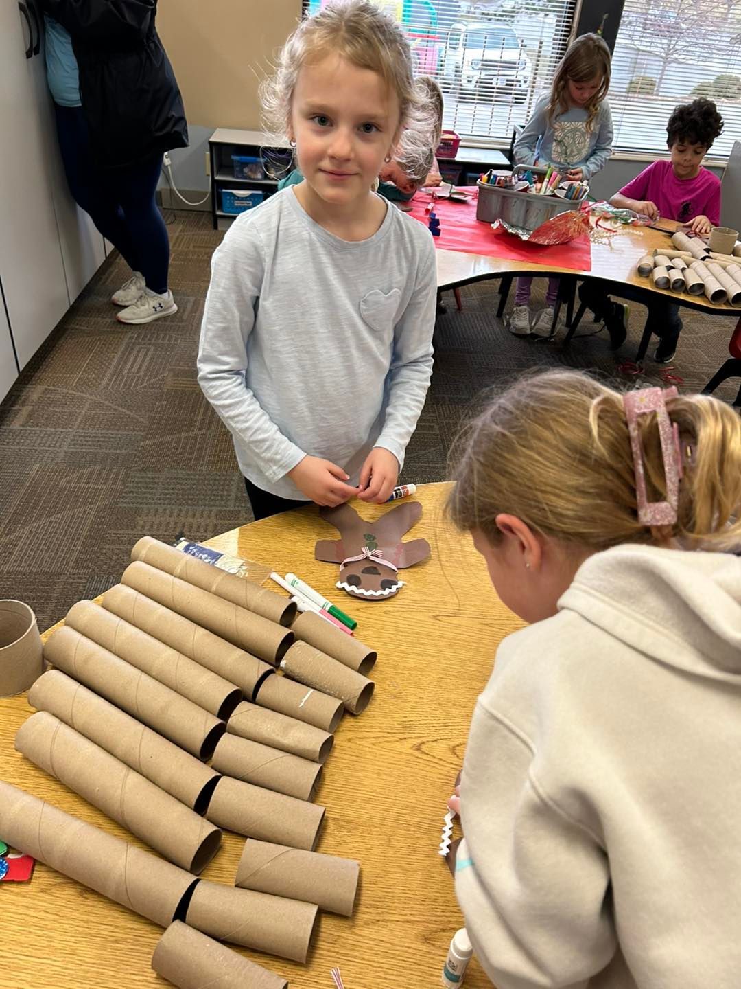 A group of young girls are sitting at a table making crafts out of toilet paper rolls.