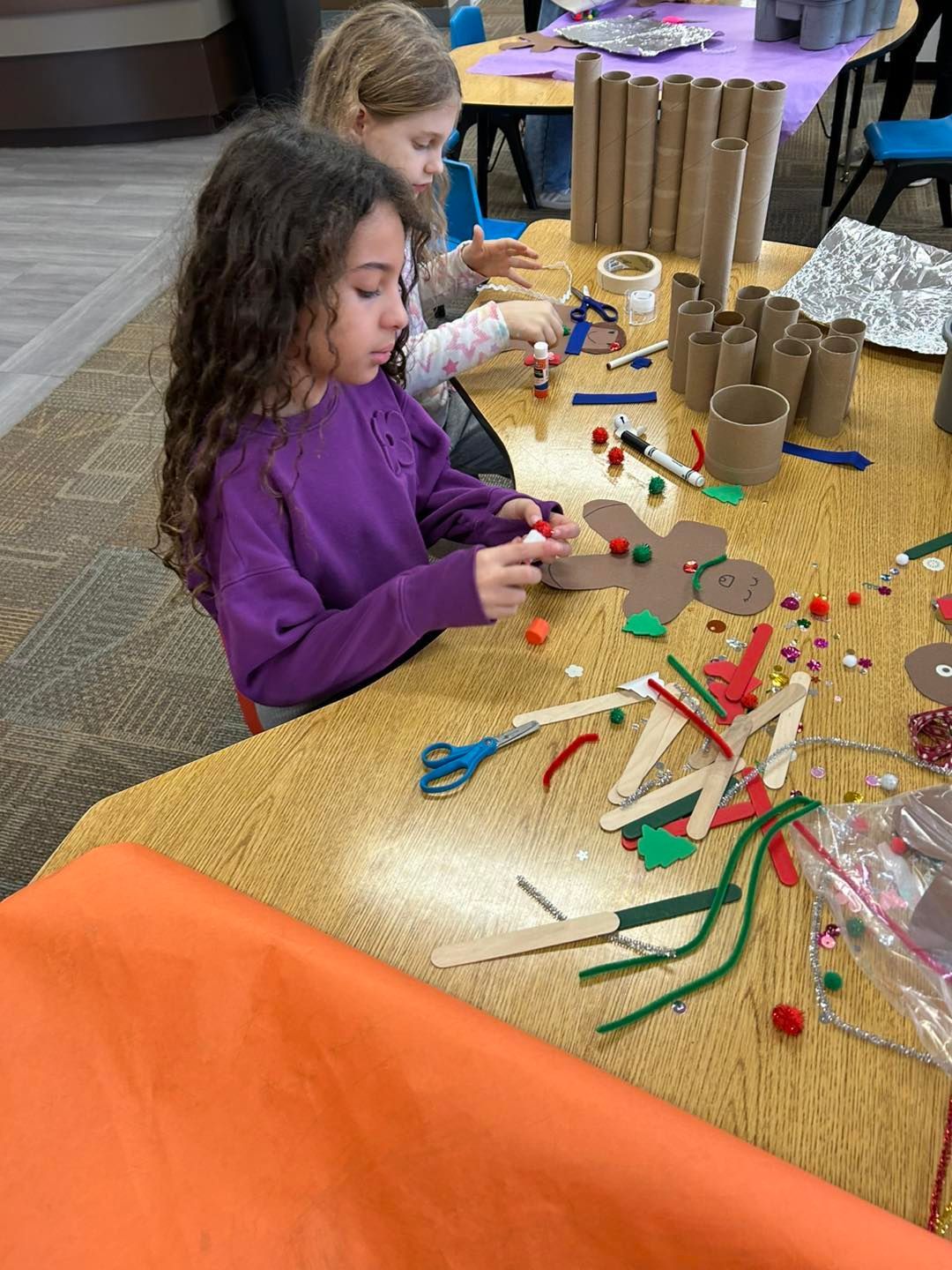 Two young girls are sitting at a table making crafts out of toilet paper rolls.