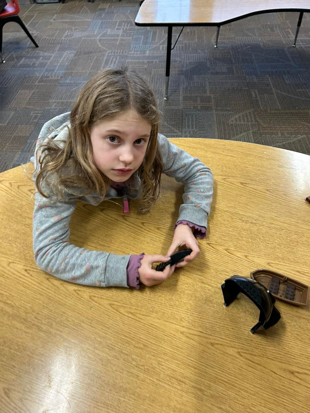 A young girl on a wooden table holding a pair of goggles.