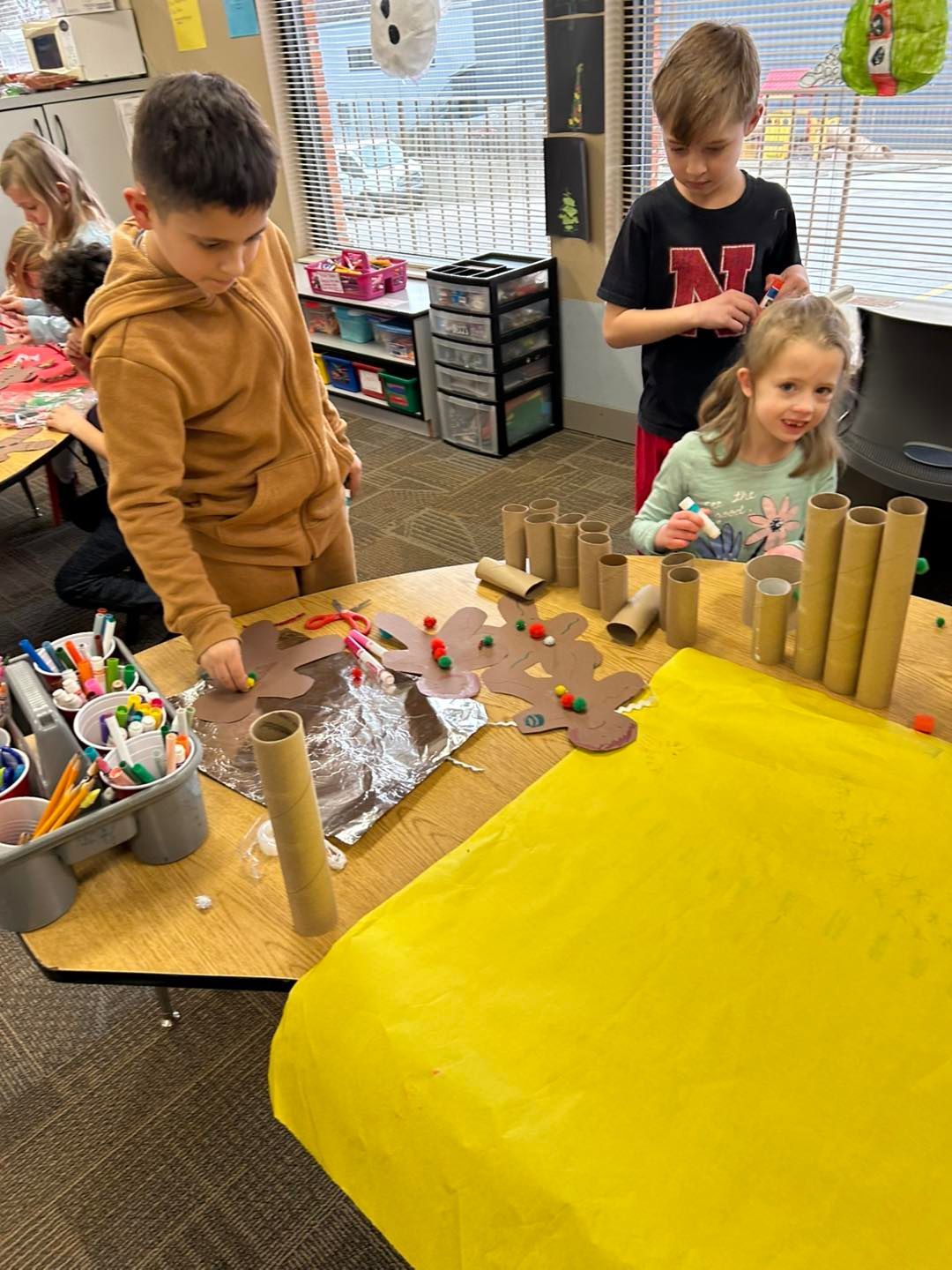 A group of children are sitting at a table making crafts out of toilet paper rolls.