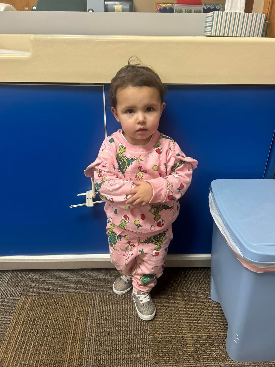 A little girl in pink pajamas is standing in front of a blue cabinet.