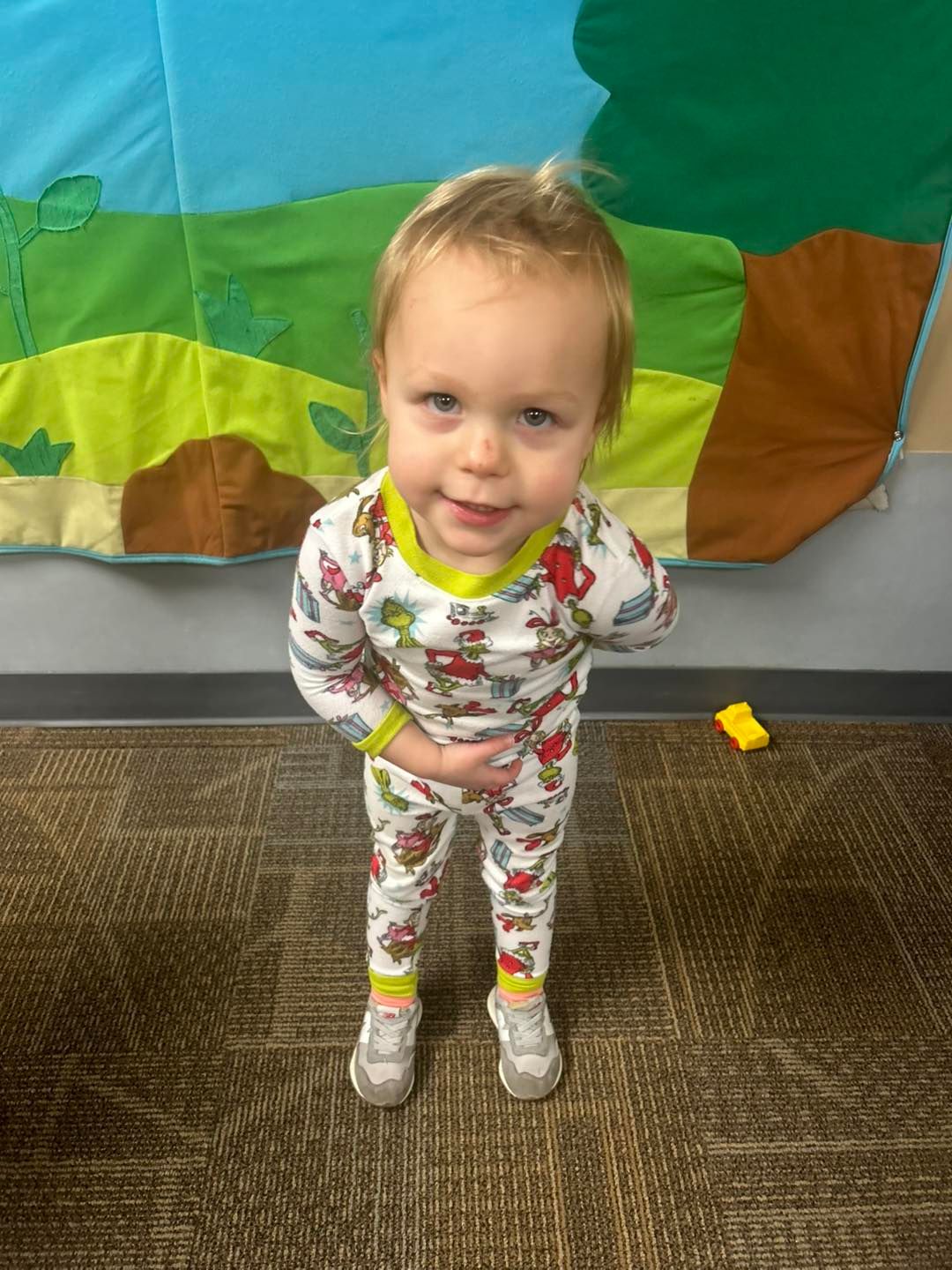 A little boy in pajamas is standing on the floor with his hands on his hips.