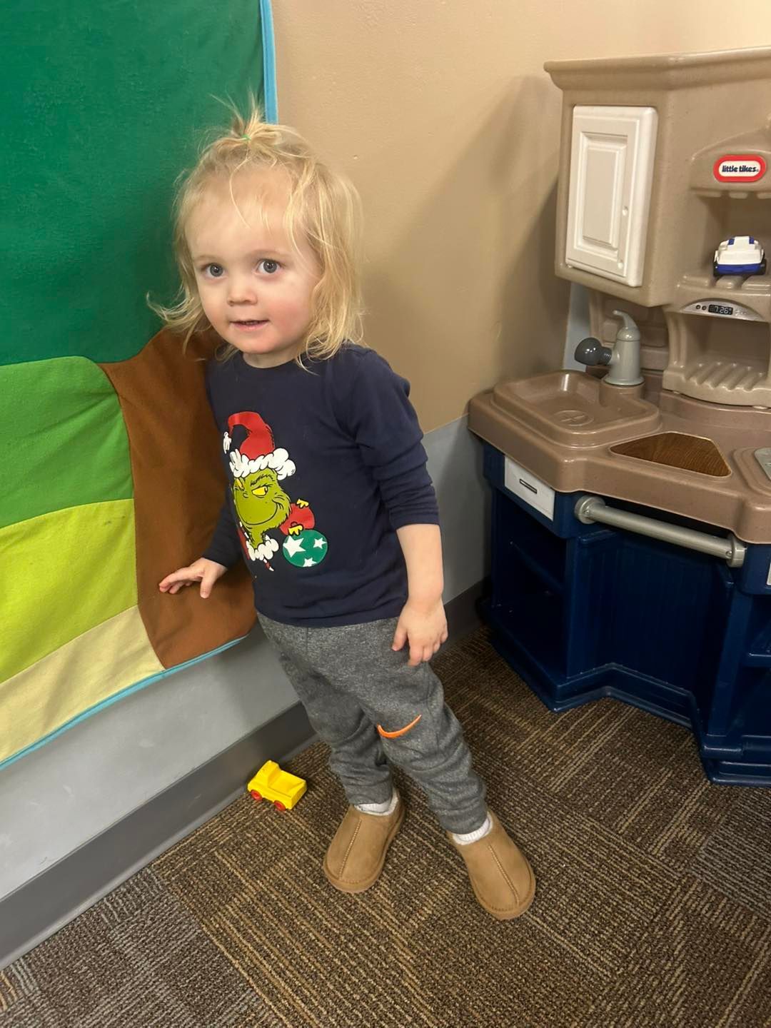 A little girl is standing in a room next to a toy kitchen.