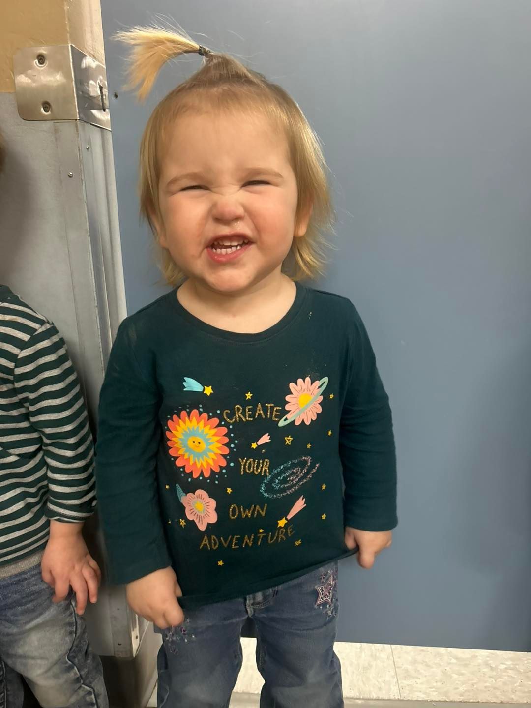 A little girl wearing a green shirt that says create your own adventure