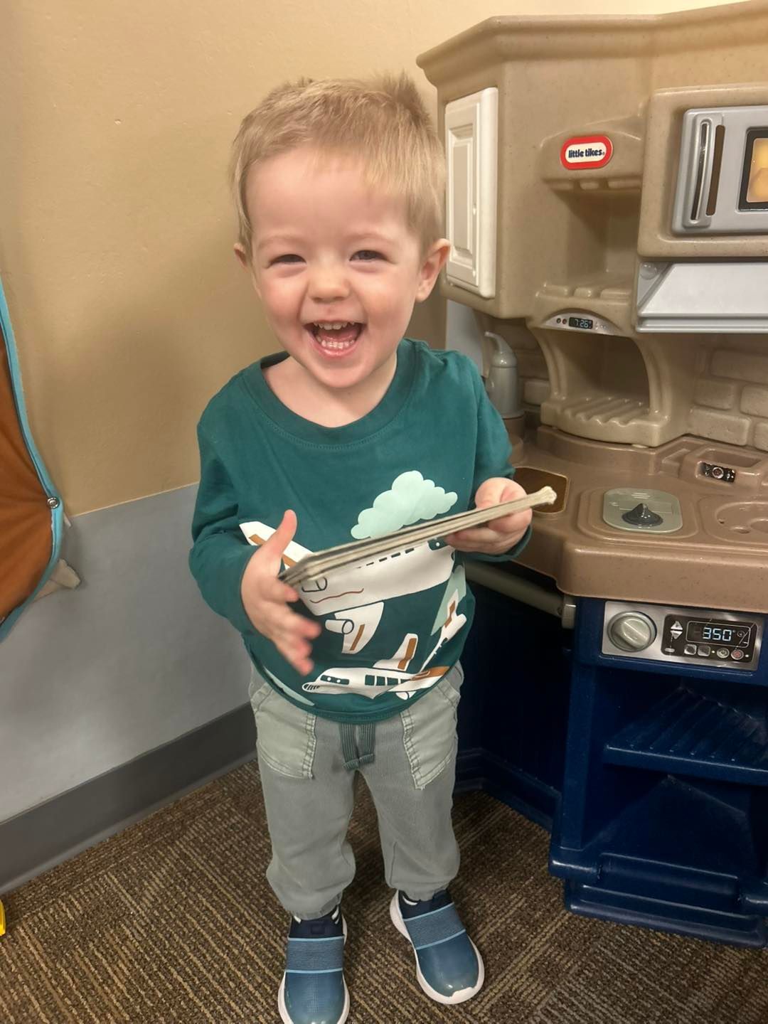 A little boy is standing in front of a play kitchen.