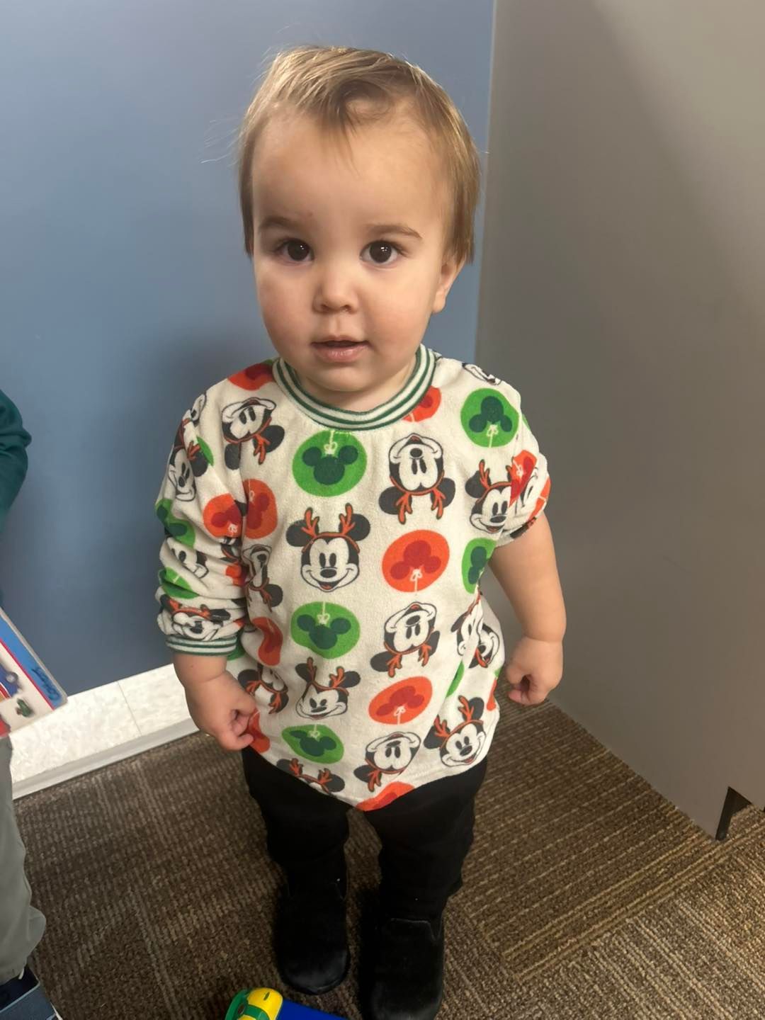 A child wearing a mickey mouse shirt is standing on a carpet.