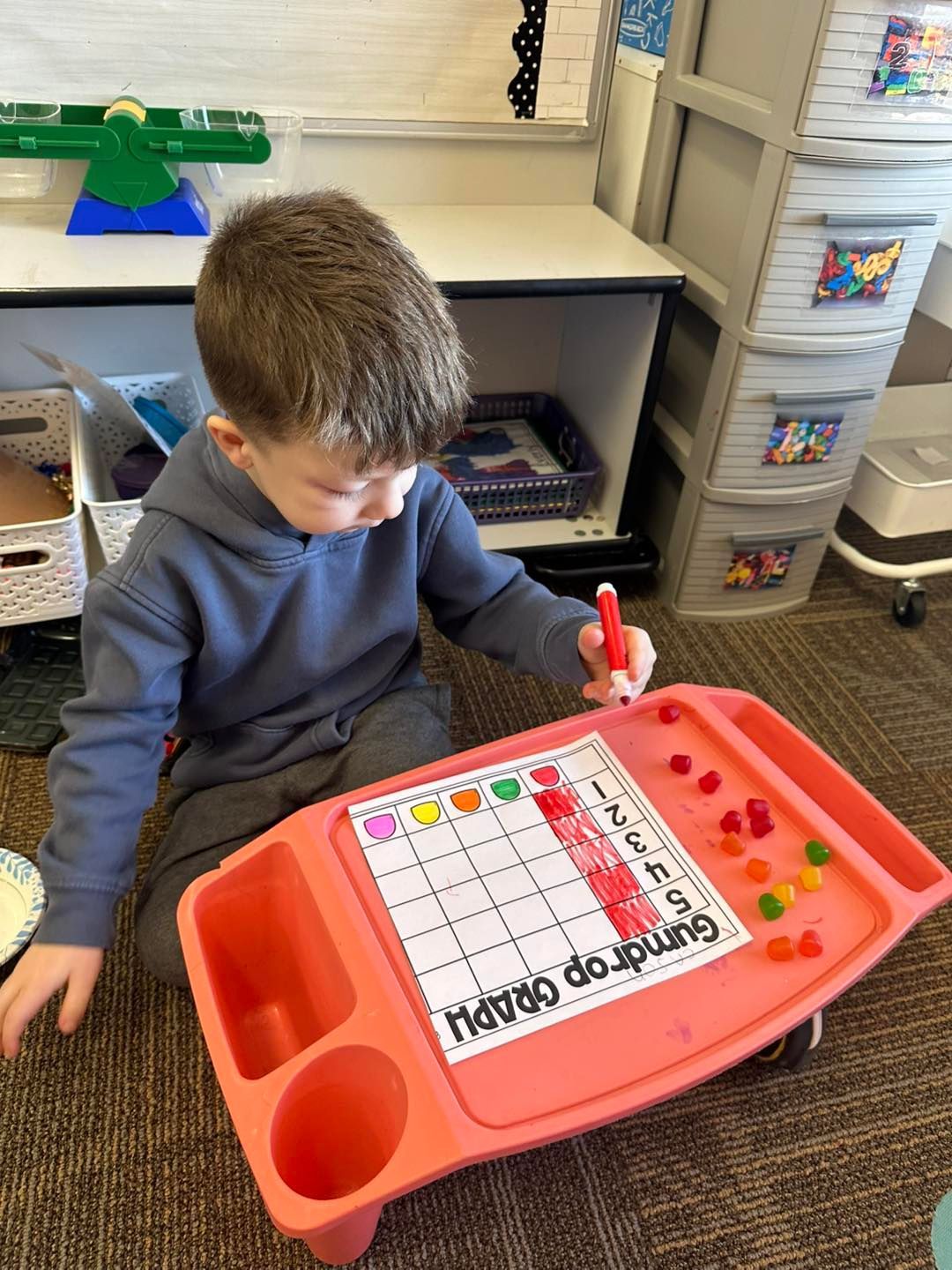A young boy is sitting on the floor playing with a table with gummy bears on it.