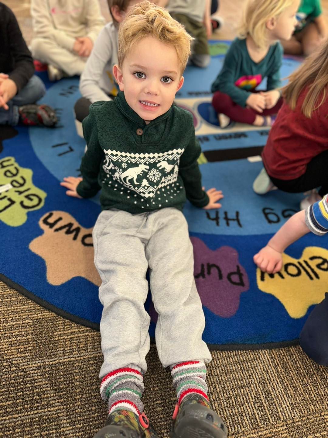 A young boy is sitting on the floor wearing a green sweater